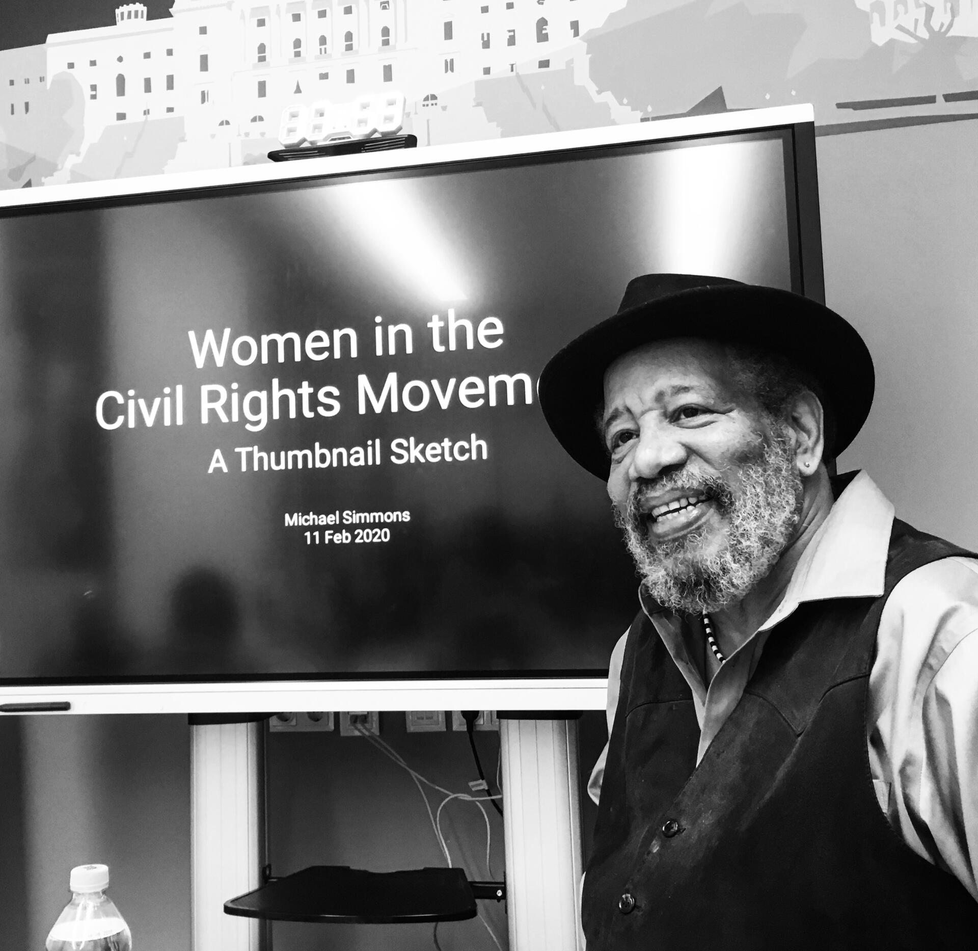 Michael Simmons standing in front of a digital screen with a presentation title slide displayed
